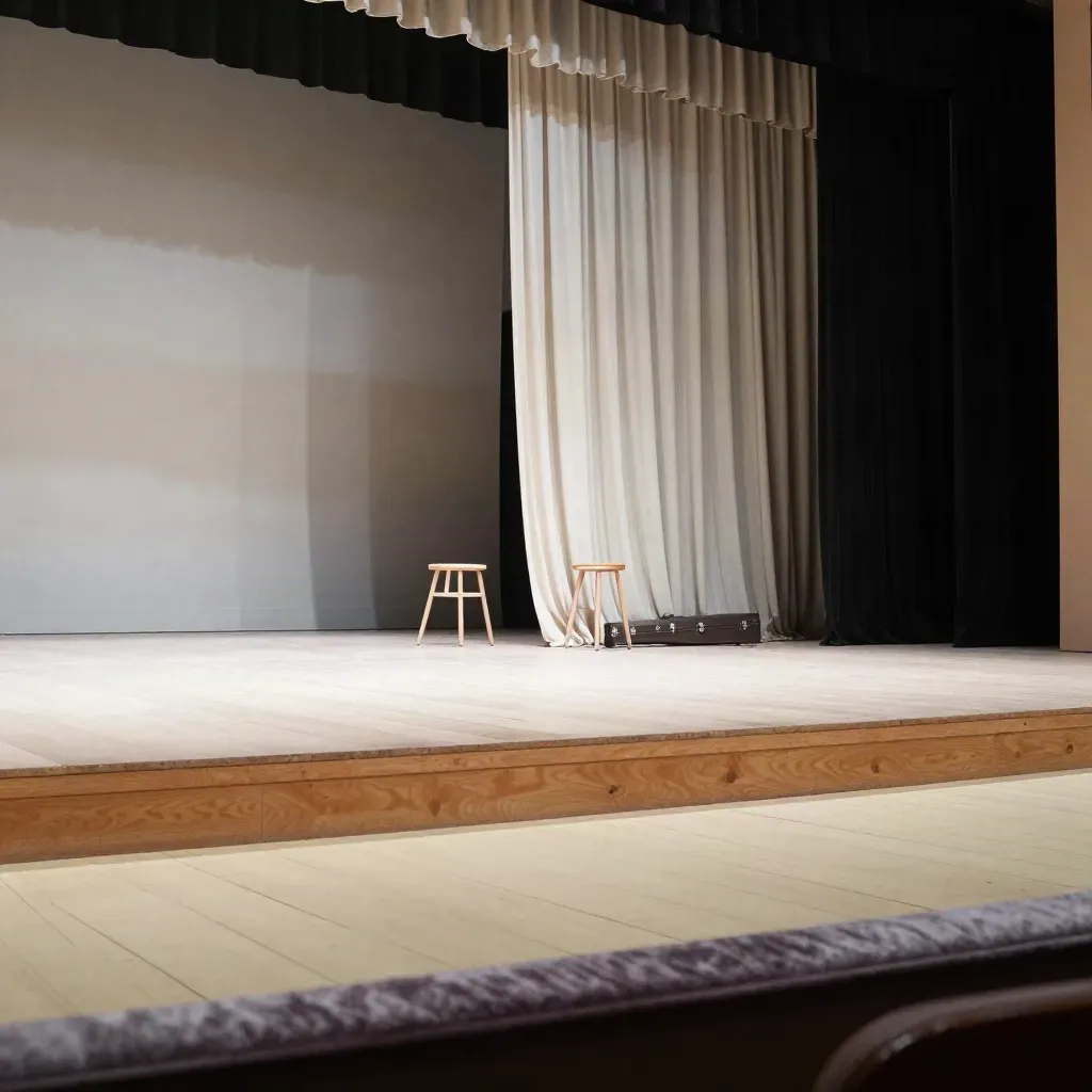 Leere Theaterbühne mit halb offenem Vorhang, Hocker und Instrumentenkoffer im Seitenlicht.